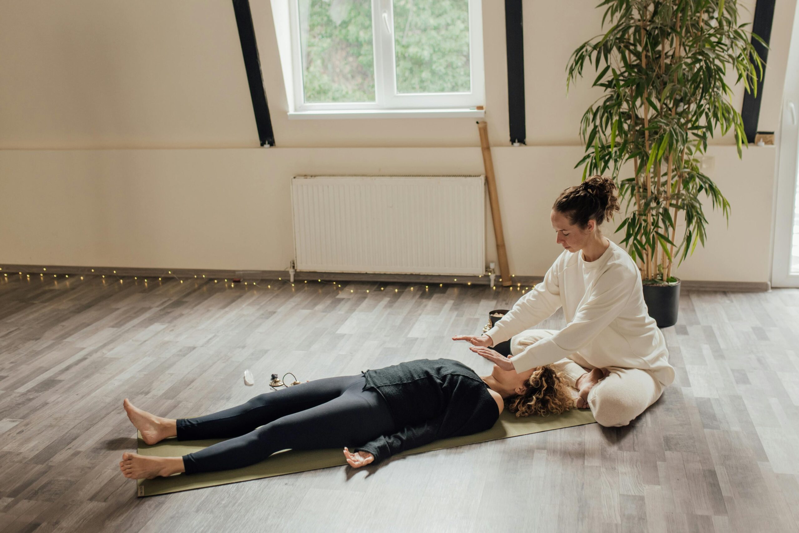 A serene indoor scene of a Reiki healing session with two women on a yoga mat for relaxation and wellness.